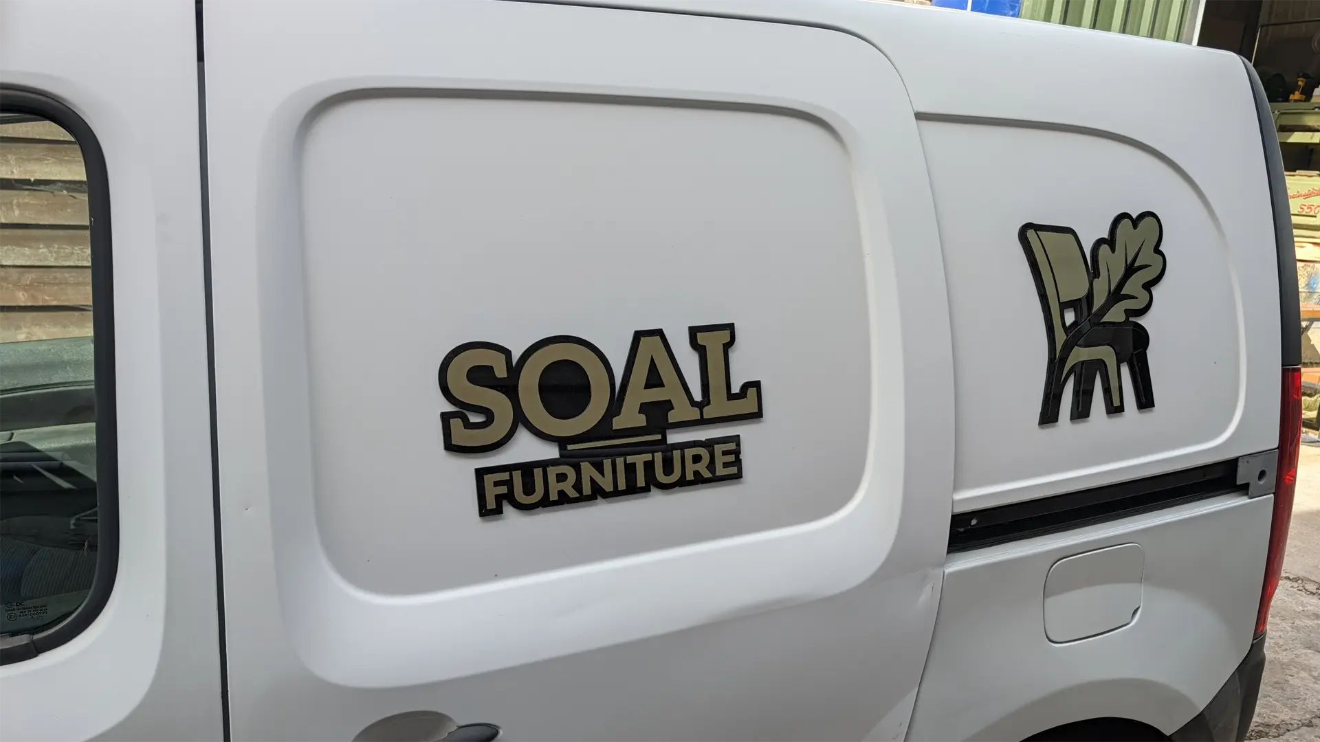 Black and gold 3D acrylic SOAL Furniture logo and chair emblem installed on the van