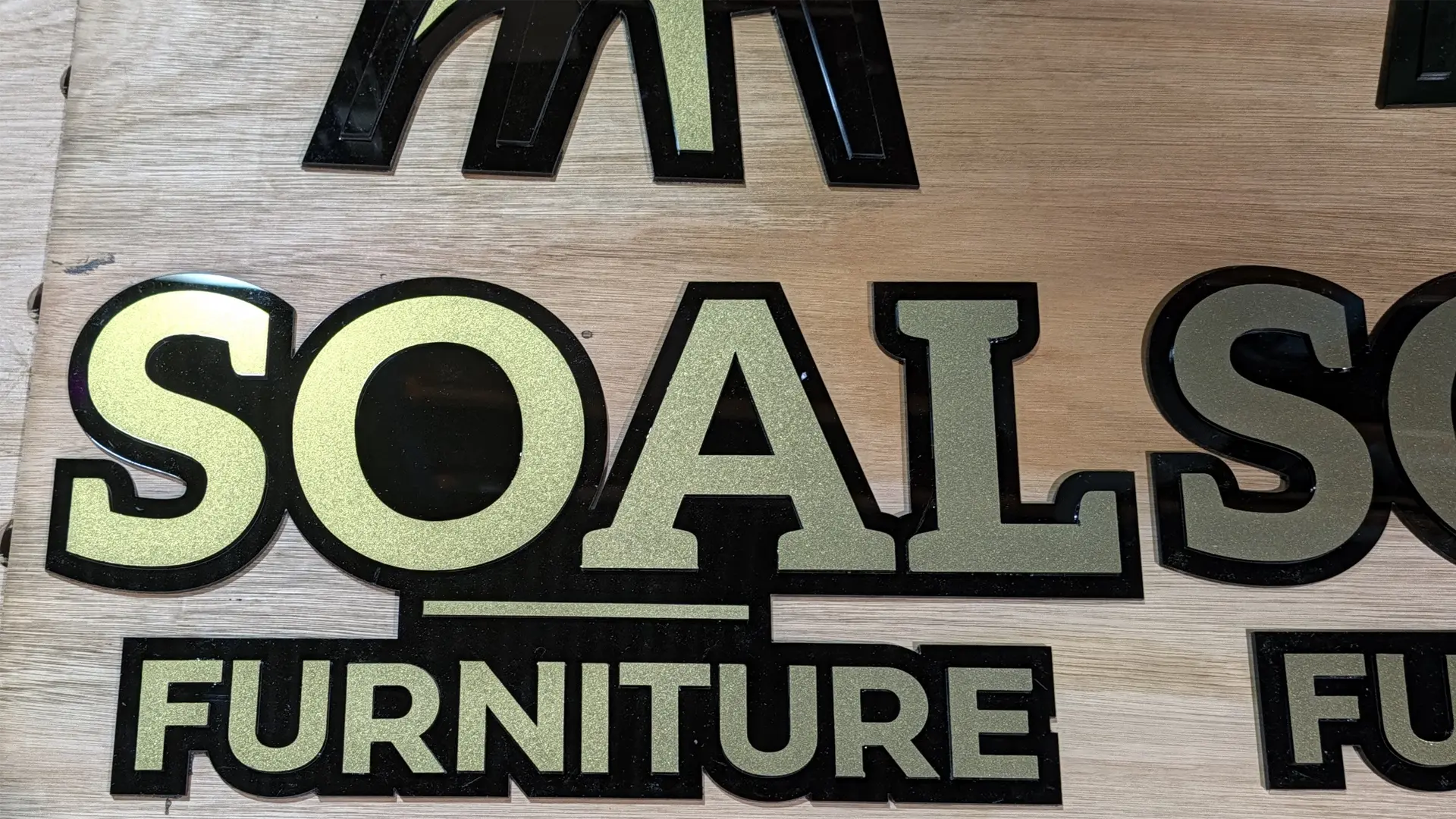 Layered black and gold SOAL Furniture acrylic logo assembled on the workshop bench